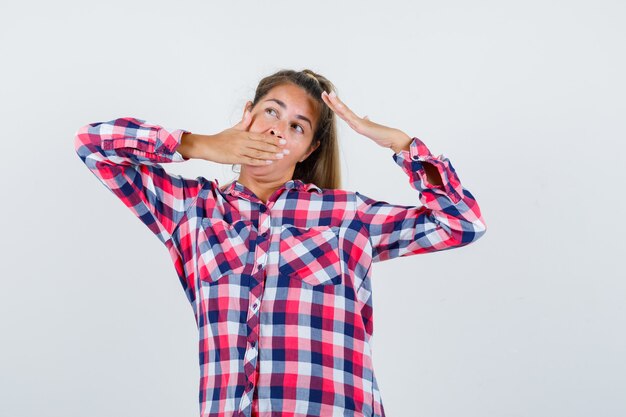 Jeune femme bâillant tout en étirant le haut du corps en chemise à carreaux et à l'air détendu. vue de face.