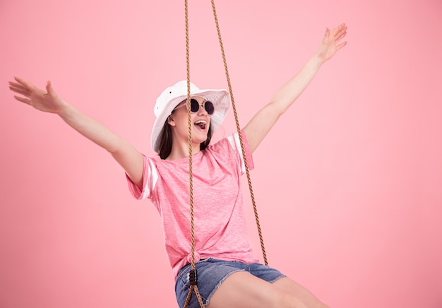 Jeune femme sur une balançoire sur fond rose.