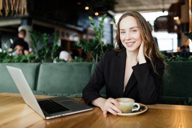 Jeune femme de beauté travaillant à l'ordinateur portable dans un café