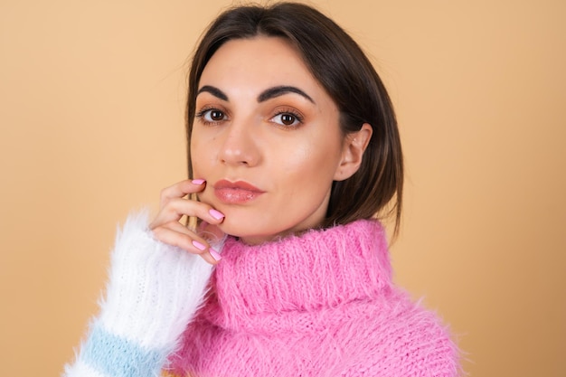 Jeune femme sur beige dans un pull tricoté confortable multicolore lumineux mignon souriant