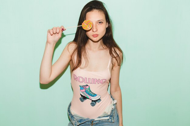 Jeune femme belle hipster posant contre le mur bleu, tenant des bonbons sucette pop