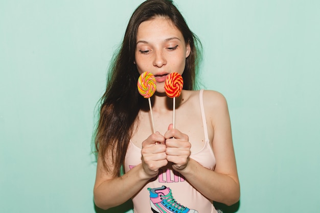 Jeune femme belle hipster posant contre le mur bleu, tenant des bonbons sucette pop