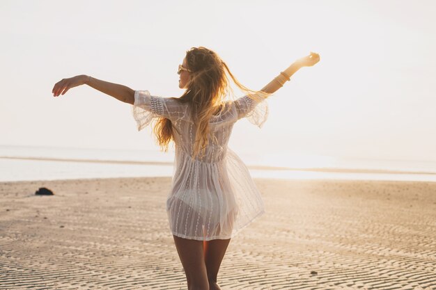 Jeune femme belle mince sur la plage au coucher du soleil