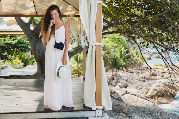 Jeune femme belle naturelle en robe pâle posant sous chapiteau, vacances tropicales,