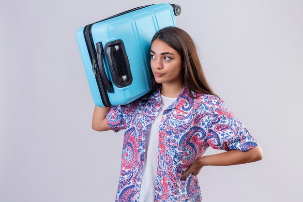 Jeune femme belle voyageur debout avec valise sur l'épaule mécontent à côté sur fond blanc isolé