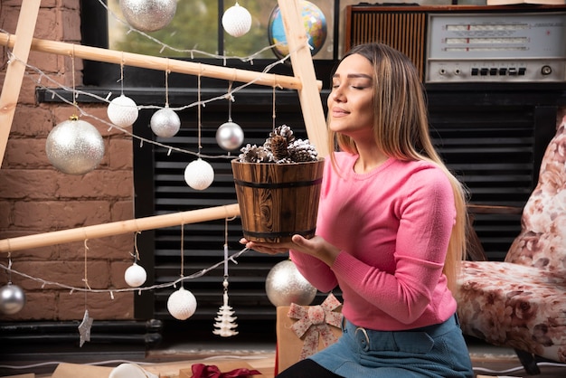 Jeune femme bénéficiant d'un seau de pommes de pin à la maison.