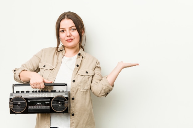 Jeune femme bien roulée tenant une radio rétro montrant un espace de copie sur une paume et tenant une autre main sur la taille