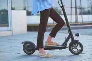 Photo gratuite jeune femme en blaser dépouillé monte son nouveau scooter électrique dans la rue.