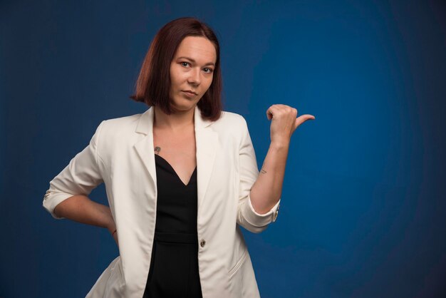 Jeune femme en blazer blanc faisant bon signe.