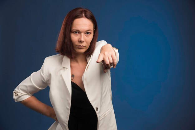 Jeune femme en blazer blanc vous pointant.