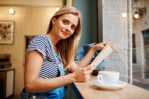 Jeune femme blonde assise dans le café et la lecture