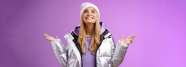 Photo gratuite une jeune femme blonde attrayante avec un chapeau d'hiver, une veste argentée à la mode, lève la main.