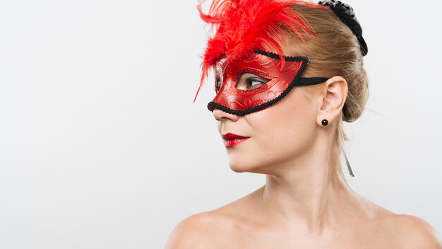 Jeune femme blonde au masque avec des plumes rouges