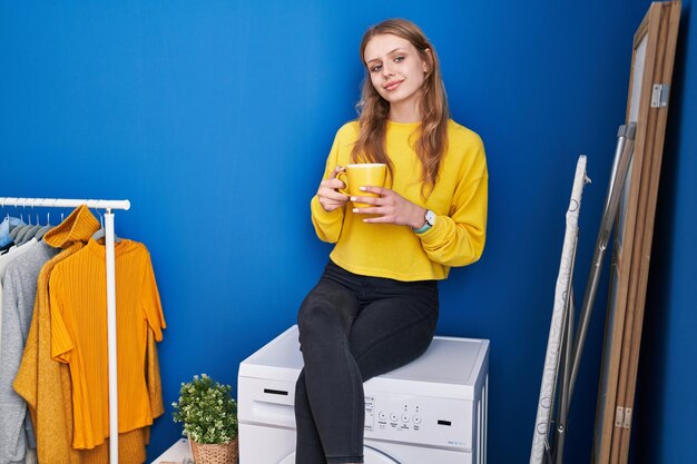 Photo gratuite jeune femme blonde buvant du café en attendant la machine à laver à la buanderie