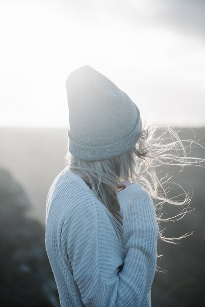 Jeune femme blonde avec un chapeau marchant sur la plage par temps venteux