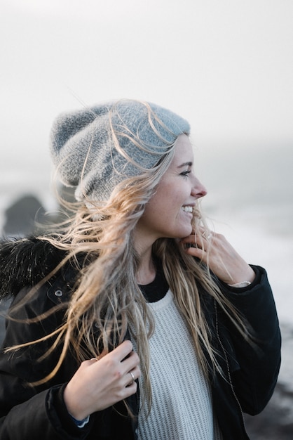 Jeune femme blonde avec un chapeau s'amusant sur la plage par temps venteux