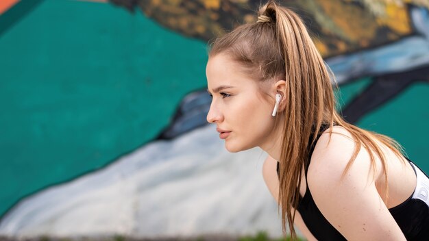 Jeune femme blonde concentrée à la formation en plein air au repos après l'exécution, fond multicolore