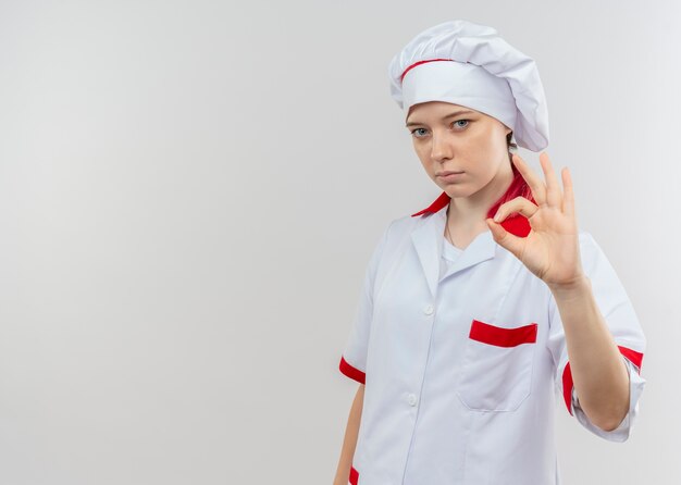 Jeune femme blonde confiante chef en uniforme de chef gestes signe de la main ok isolé sur mur blanc