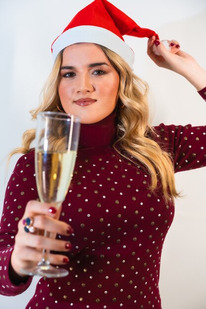 Jeune femme blonde dans un bonnet de Noel posant avec un verre de champagne