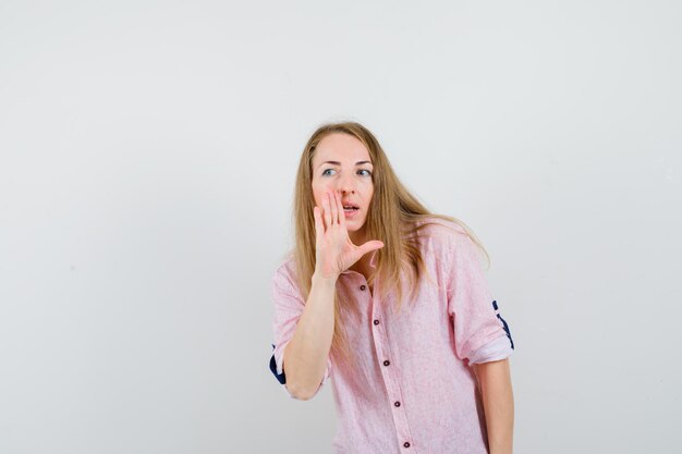 Jeune femme blonde dans une chemise rose décontractée chuchotant