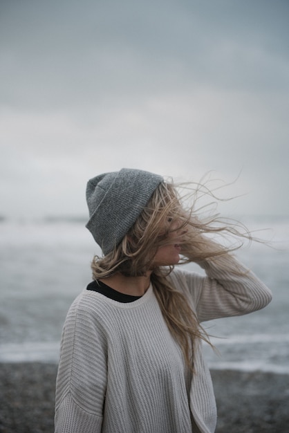 Jeune femme blonde en dépression avec un chapeau marchant sur la plage par temps venteux