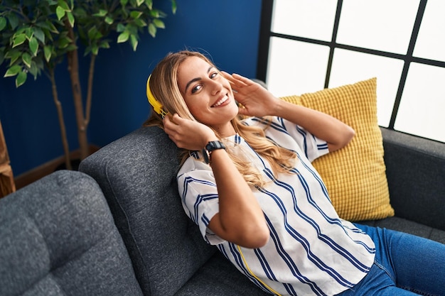 Jeune femme blonde écoutant de la musique détendue sur un canapé à la maison