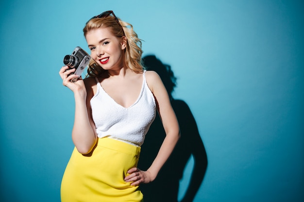 Jeune femme blonde élégante à lunettes de soleil tenant un appareil photo rétro
