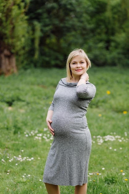 Jeune femme blonde enceinte en robe grise, fille enceinte au printemps sur une promenade, concept de maternité