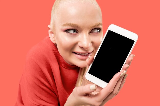 Jeune femme blonde sur fond de corail avec smartphone