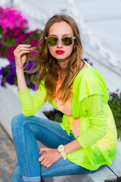 Jeune femme blonde hipster élégant dans des lunettes de soleil cool avec cocktail posant en plein air
