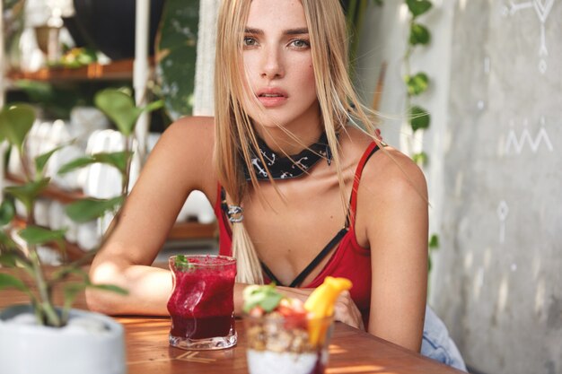 Jeune femme blonde avec des lunettes de soleil élégantes rouges posant dans un café