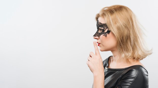 Jeune femme blonde en masque avec un doigt près des lèvres