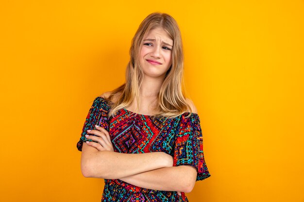 Jeune femme blonde mécontente debout avec les bras croisés et regardant de côté