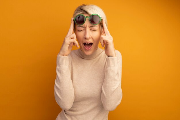 Photo gratuite jeune femme blonde portant des lunettes de soleil les élevant avec les yeux fermés et la bouche ouverte