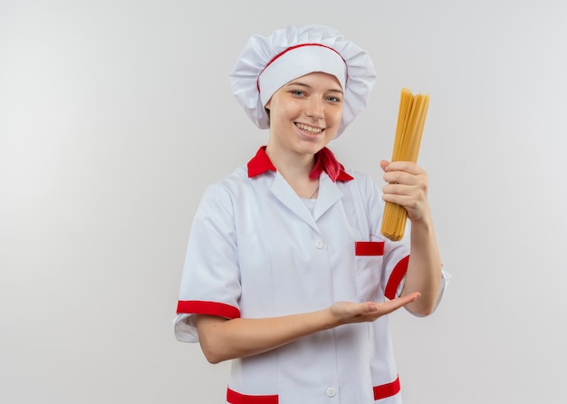 Jeune femme blonde souriante chef en uniforme de chef détient bouquet de spaghettis isolé sur mur blanc