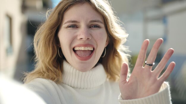 Jeune femme blonde souriante confiante ayant un appel vidéo dans la rue