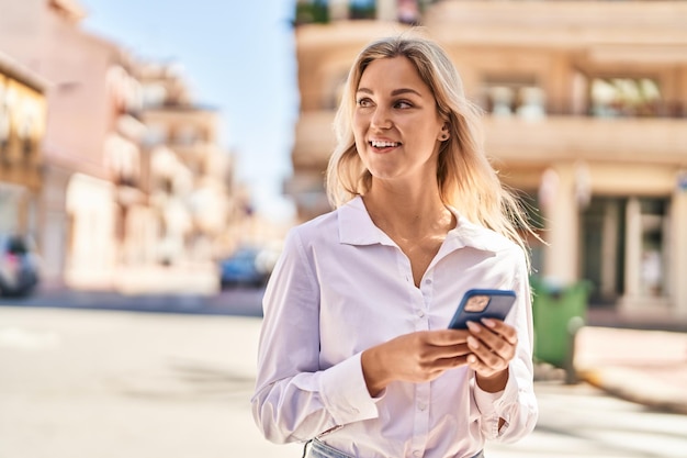 Jeune femme blonde souriante confiante utilisant un smartphone dans la rue