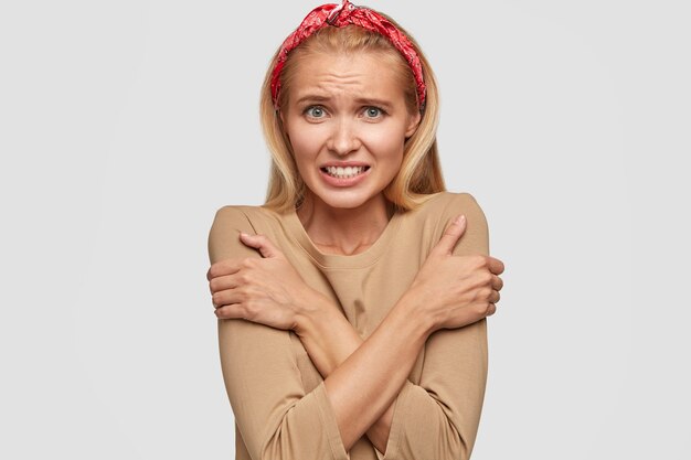 Jeune femme blonde stressante posant contre le mur blanc