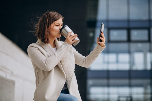 Jeune, femme, boire, café, utilisation, téléphone, dehors, rue