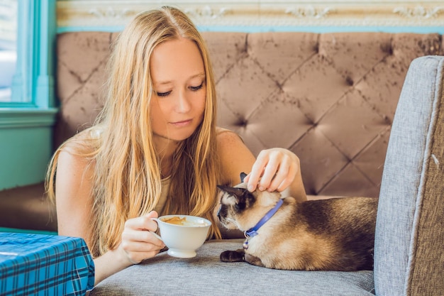 La jeune femme boit du café et caresse le chat.