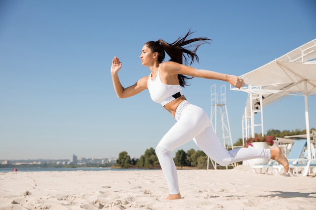 Jeune femme en bonne santé en cours d'exécution et faisant des mouvements brusques à la plage.