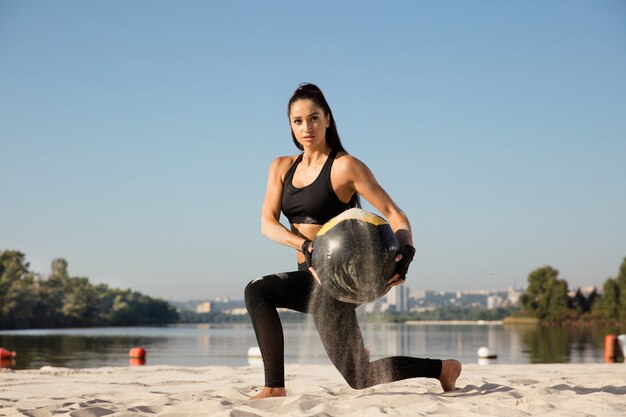 Jeune femme en bonne santé faisant des mouvements brusques avec ballon à la plage