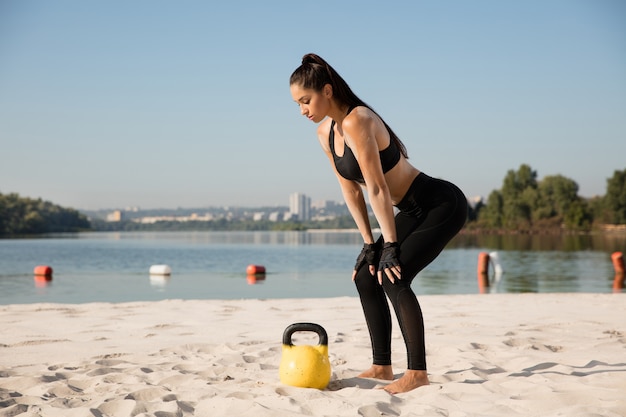 Jeune femme en bonne santé faisant des squats avec des poids à la plage.