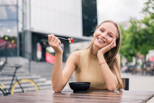 Jeune femme en bonne santé mangeant de la salade en plein air dans un café de la rue