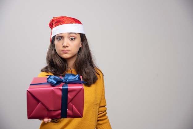 Jeune femme en bonnet de Noel montrant une boîte-cadeau.