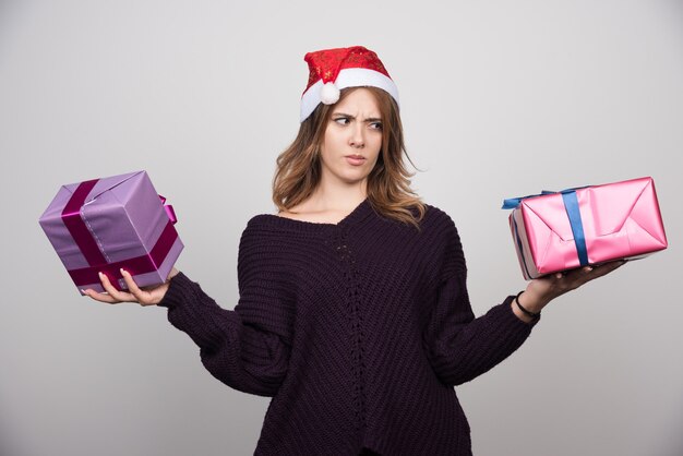 Jeune femme avec bonnet de Noel tenant des coffrets cadeaux.