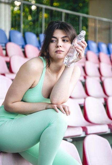 Photo gratuite une jeune femme avec une bouteille d'eau à l'entraînement au stade