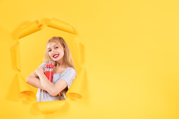 Jeune femme avec une bouteille rouge sur un mur jaune