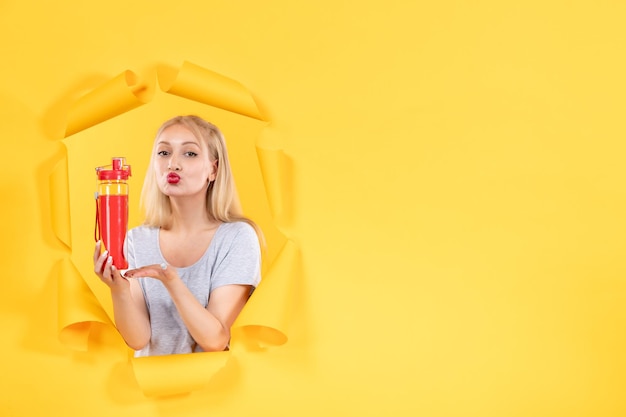 Jeune femme avec une bouteille rouge sur une surface jaune