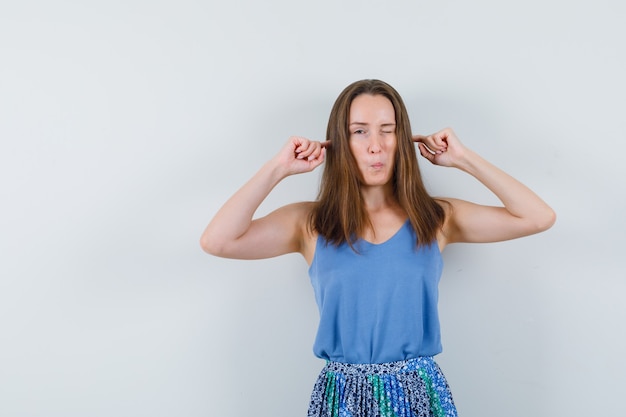 Jeune femme brancher les oreilles avec les doigts en maillot, jupe et à la curiosité